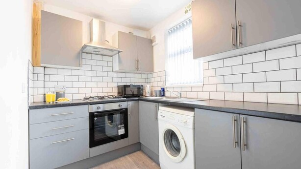 A modern kitchen with grey cabinets, a built-in oven, a microwave, and a washing machine.