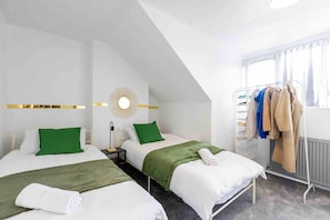 A hotel room with two beds, a wall-mounted light fixture, a radiator, and a clothing rack.
