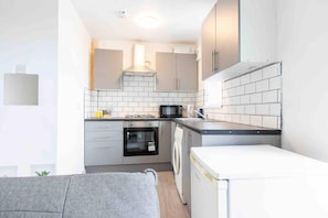 A compact kitchen with grey cabinets, a microwave, an oven, and a washing machine.