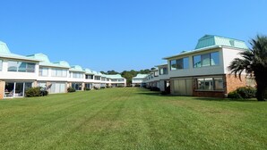 Una hilera de casas móviles modernas de dos pisos, con amplios ventanales y techo plano, ubicada en un área verde bajo un cielo azul despejado.