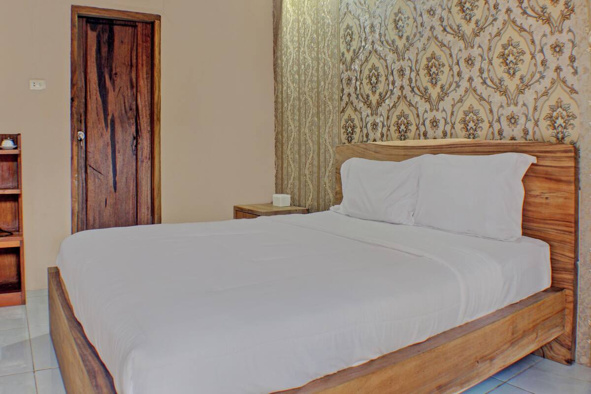 A wooden bed with white bedding in a room with patterned wallpaper and a wooden door.