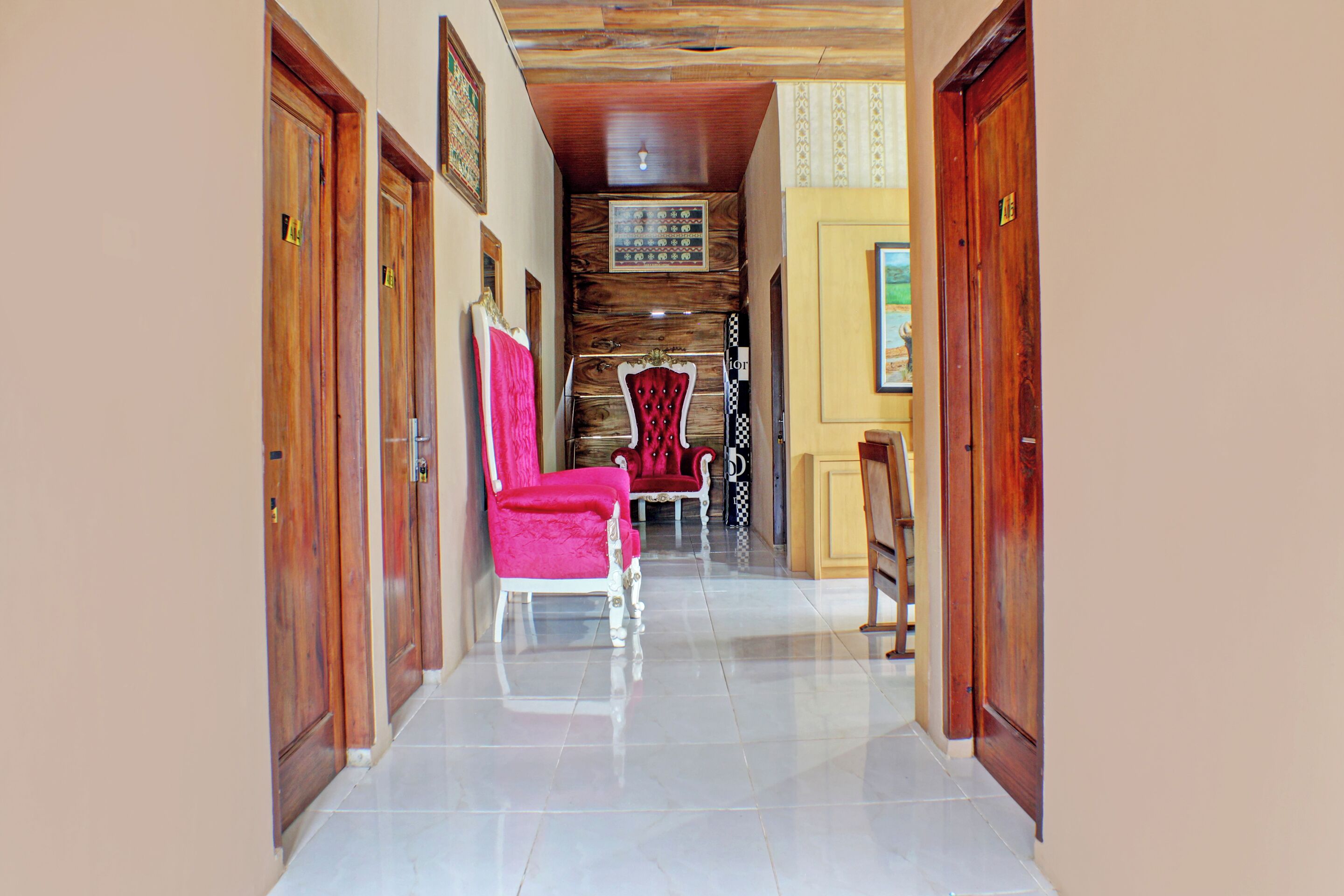 Un pasillo con puertas de madera, suelo de baldosas y una zona de estar con sillas rojas.