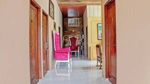 Un couloir avec des portes en bois, un sol carrelé et un espace détente avec des chaises rouges.