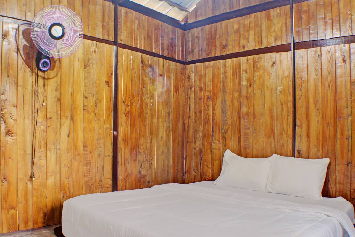 A room with wooden panel walls, a bed with white bedding, and a ceiling fan.