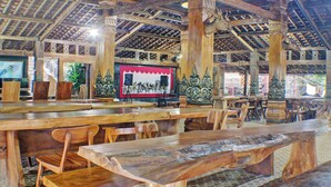 Un intérieur en bois, doté de hauts plafonds et de sculptures complexes, avec des tables et des chaises disposées pour les repas.