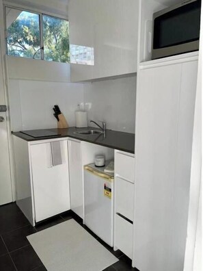 Compact kitchen with a sink, faucet, microwave, and window.