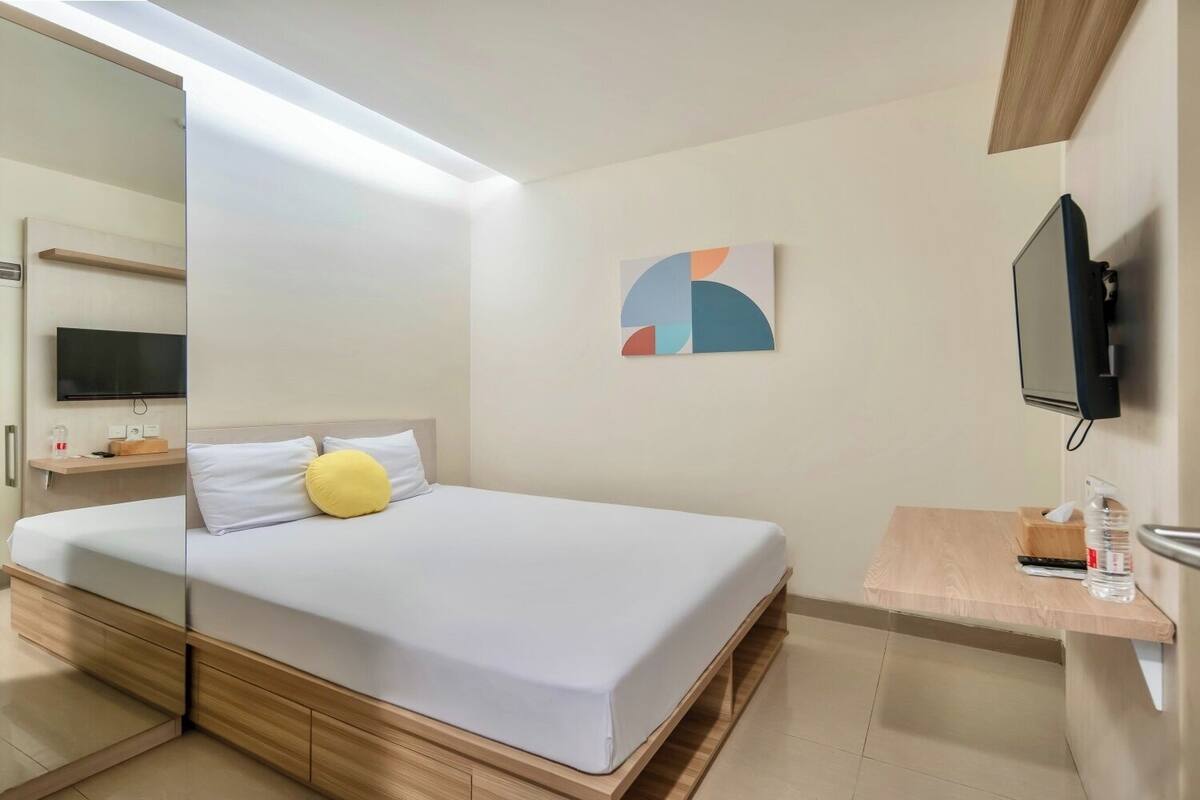 A modern hotel room with a bed, bedside table, TV, and a mirror.