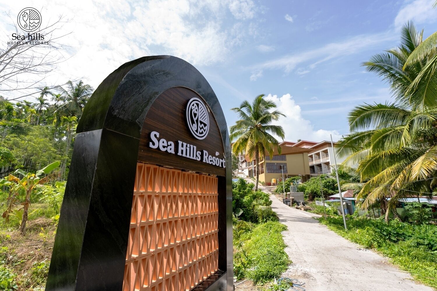 A large, arched entrance sign for Sea Hills Resort with a tropical garden path leading to the buildings.