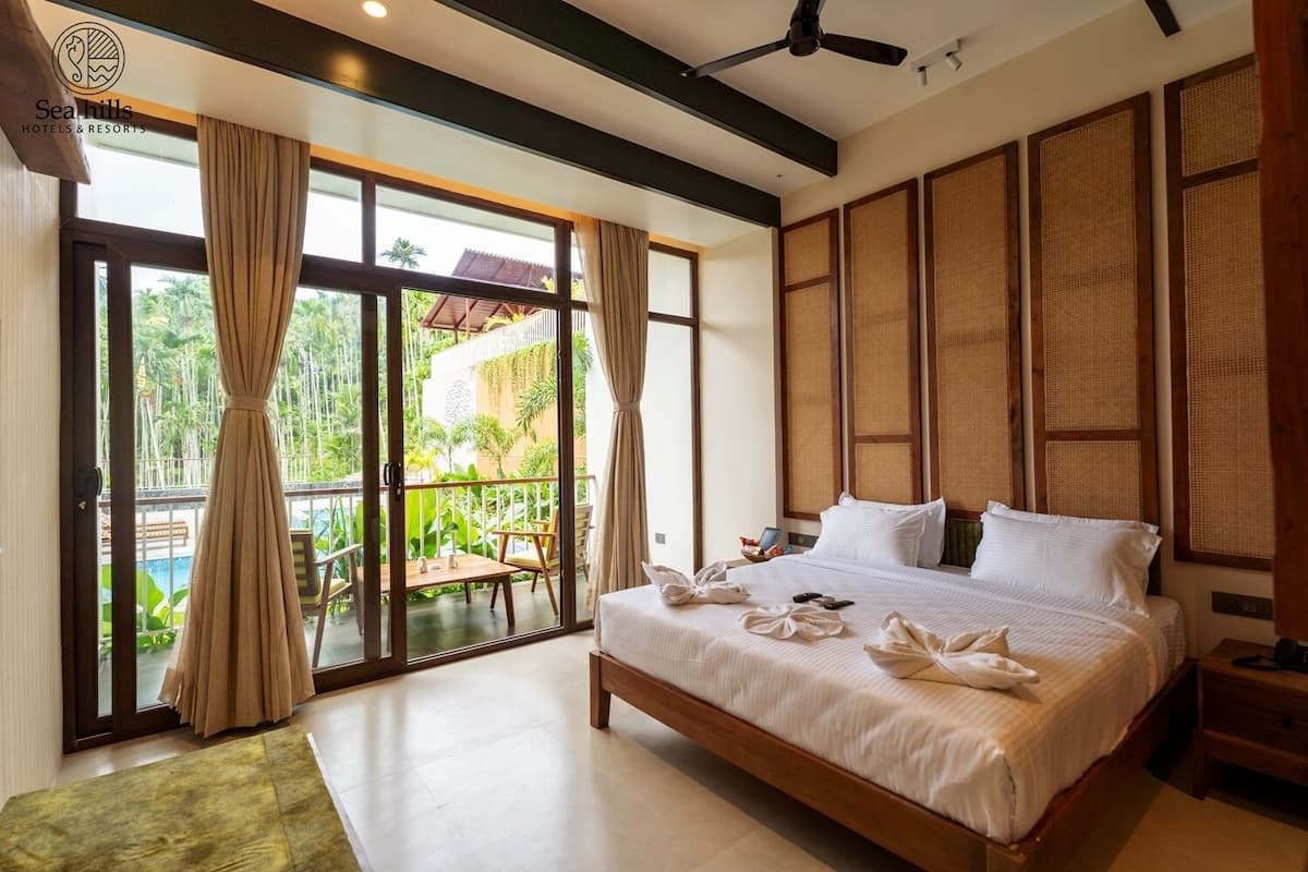A hotel room with a large bed, a balcony with curtains, and a view of a pool and greenery.