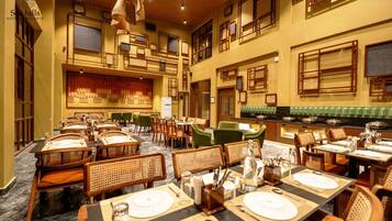 Un vaste espace dédié à la salle à manger, avec de nombreuses tables et chaises, un plafond haut orné de poutres en bois et des fenêtres de style asiatique traditionnel.
