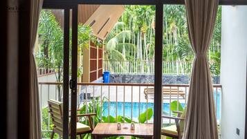 A room with a view of a pool, wooden furniture, and a tropical garden.