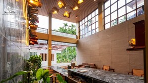 A spacious indoor area with a long dining table, multiple seating arrangements, and large windows providing natural light. - Sea Hills Resort Havelock (Port Blair)