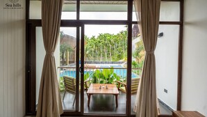 A room with a sliding glass door leading to a pool area, featuring a wooden table and chairs. - Sea Hills Resort Havelock (Port Blair)
