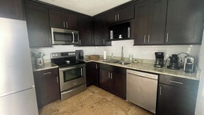 A kitchen with dark cabinets, stainless steel appliances, a microwave, stove, dishwasher, and a coffee maker.