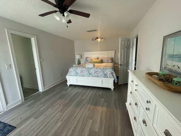 A bedroom with a bed, a ceiling fan, a nightstand, a dresser, and a painting on the wall.