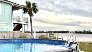 A swimming pool with a wooden deck, a covered patio, and a view of the water.