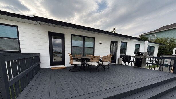 A deck with a table and chairs, a grill, and a door leading to a covered area.
