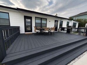 A deck with a table and chairs, a grill, and a door leading to a covered area.