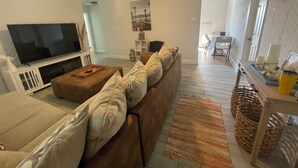 A living room with a large flat-screen TV, a brown sofa, and a wooden coffee table.