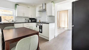A modern kitchen with white cabinets, a dark countertop, and a dining area with a wooden table and chairs. - Modern, Quiet & Comfy ~ King Beds ~ Free Parking! (LONDON)