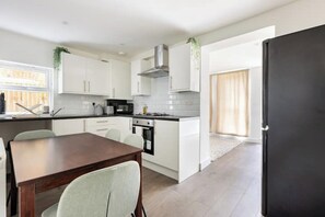 Enjoy meals in this kitchen with a dining table and chairs, stainless steel range hood, oven, and a refrigerator.