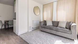 A modern living room with a grey sofa, a round mirror, and a dining area with a table and chairs. - Modern, Quiet & Comfy ~ King Beds ~ Free Parking! (LONDON)