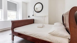 A bedroom with a wooden bed, white bedding, a round mirror on the wall, and a window with blinds. - Modern, Quiet & Comfy ~ King Beds ~ Free Parking! (LONDON)