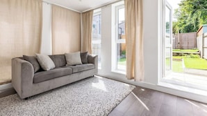 A modern living room with a grey sofa, a patterned rug, and large windows with curtains. - Modern, Quiet & Comfy ~ King Beds ~ Free Parking! (LONDON)