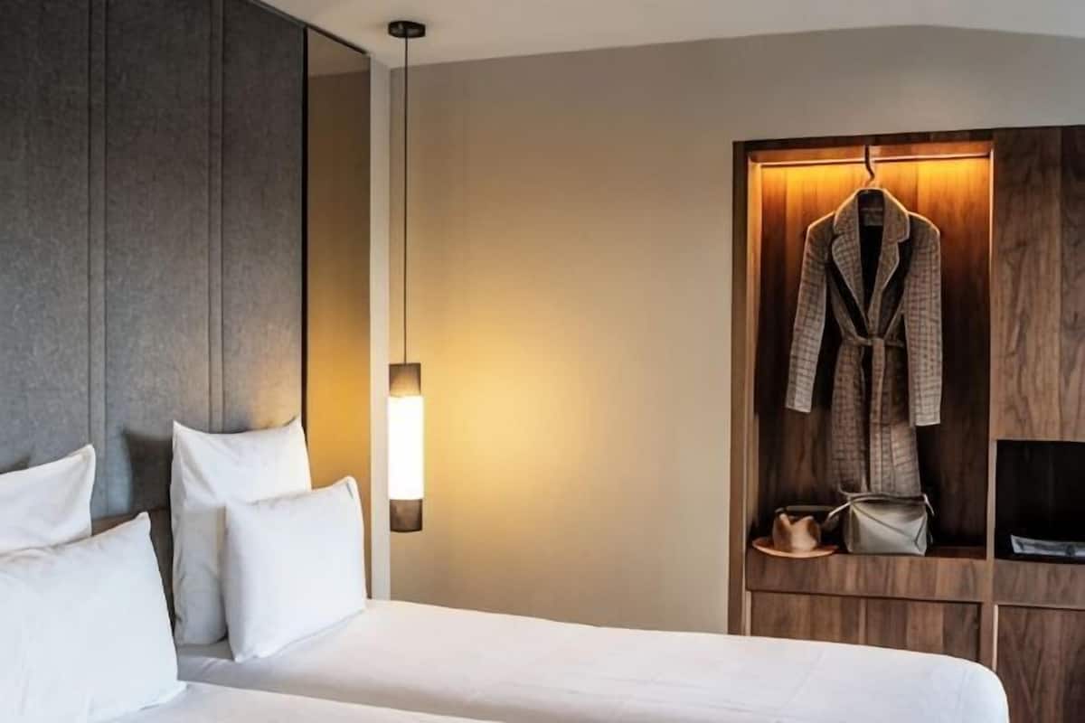 Habitación de hotel con cama, bata colgada en un estante de madera y lámpara de pared.