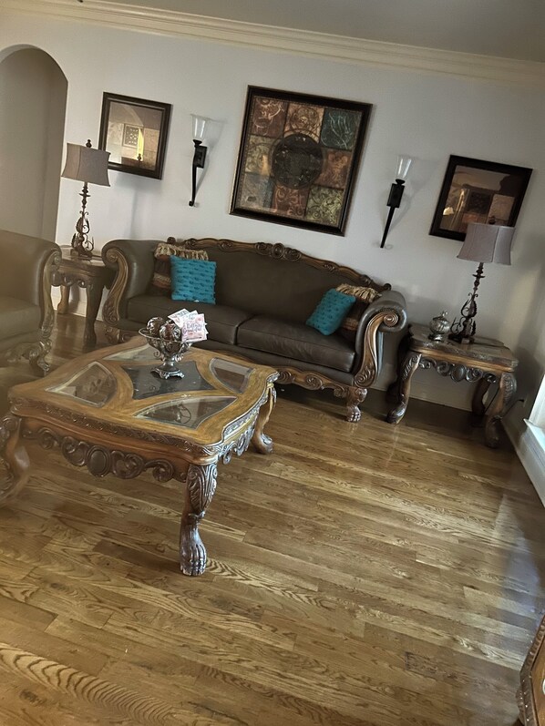 Una sala de estar con un sofá marrón, una mesa de centro de vidrio y suelo de madera.