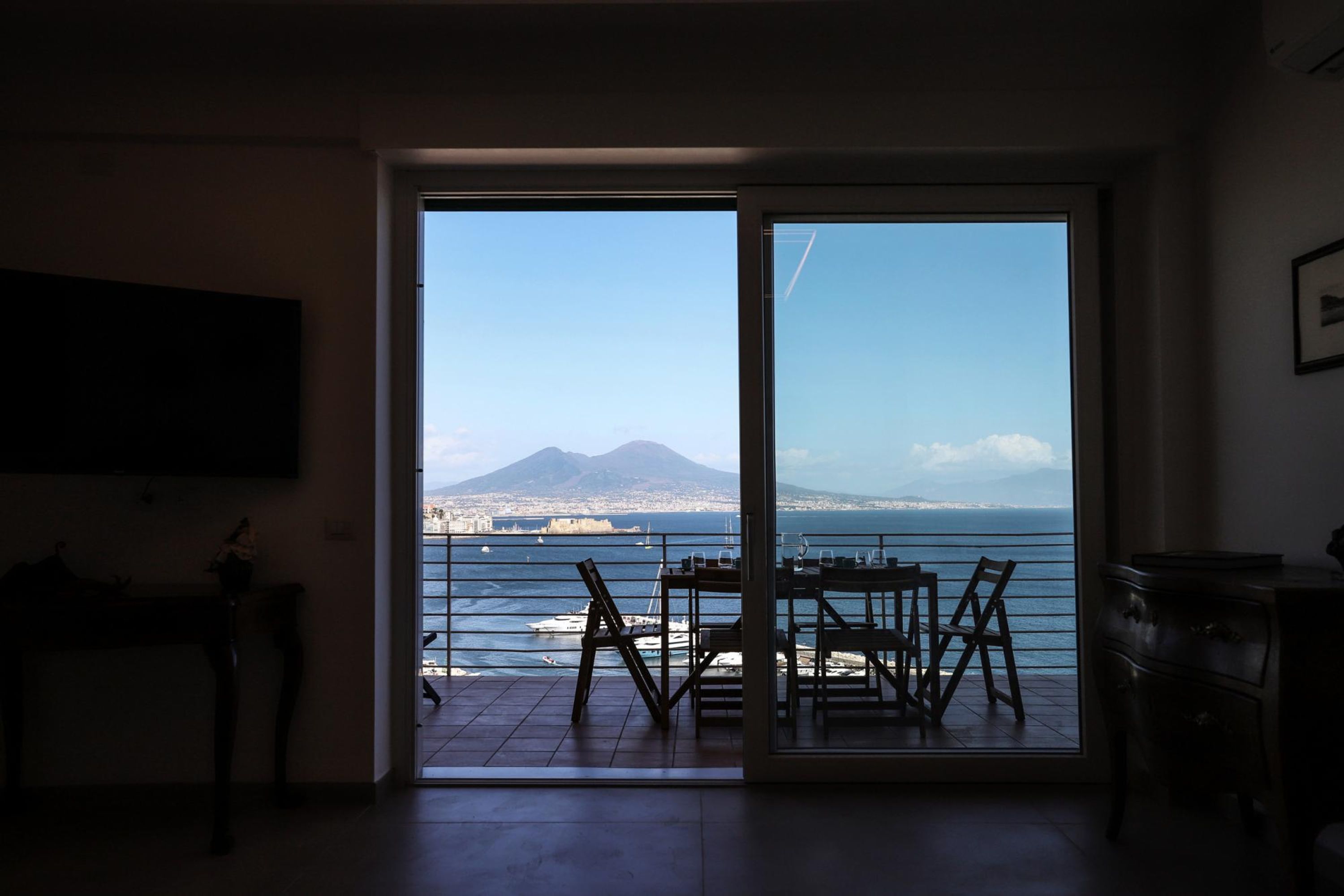 Quarto com porta de vidro deslizante para varanda com vista para a costa, barcos e montanha ao longe.