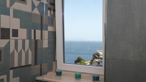 A bathroom with a window overlooking the sea, a tiled wall, and three candles on a ledge. - La Terrazza sul Golfo di Napoli by Wonderful Italy (Naples)