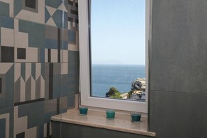 A bathroom with a window overlooking the sea, a tiled wall, and three candles on a ledge. - La Terrazza sul Golfo di Napoli by Wonderful Italy (Naples)