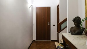 A hallway with a wooden door, a marble table with a bust sculpture, and a staircase with a railing. - La Terrazza sul Golfo di Napoli by Wonderful Italy (Naples)
