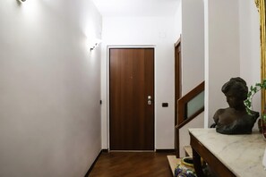 A hallway with a wooden door, a marble table with a bust sculpture, and a staircase with a railing. - La Terrazza sul Golfo di Napoli by Wonderful Italy (Naples)