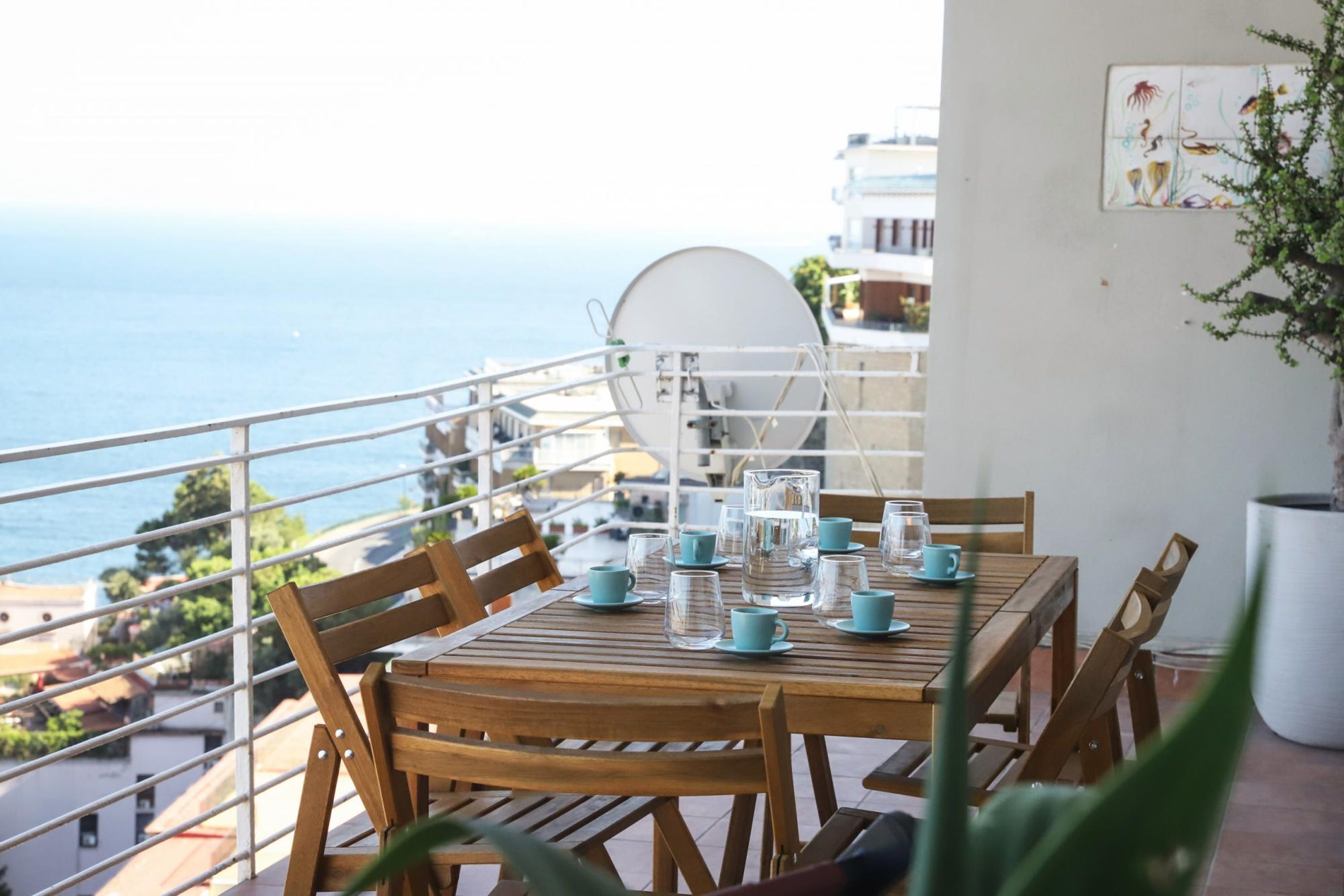 Une table en bois, dressée avec des verres transparents et des tasses bleues, offre une vue sur la côte.