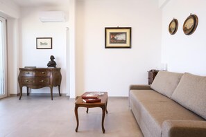 Een woonkamer met een bank, een houten salontafel, een dressoir met lades en kunstwerken in lijsten aan de muur.