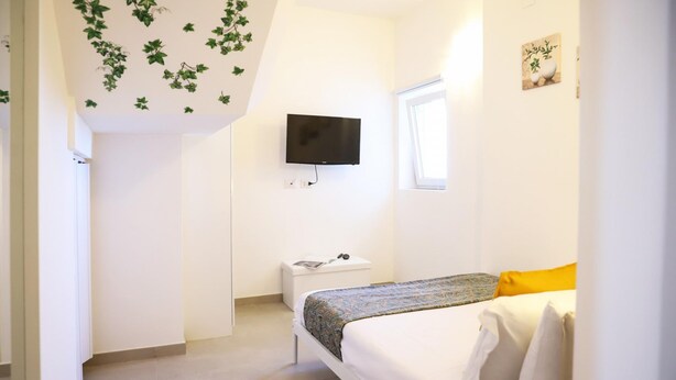 A bedroom with a bed, a television mounted on the wall, a window, and a small bedside table. - La Terrazza sul Golfo di Napoli by Wonderful Italy (Naples)