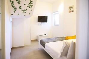A bedroom with a bed, a television mounted on the wall, a window, and a small bedside table.