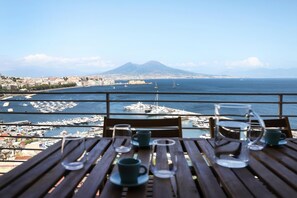 A table with empty cups and a glass pitcher, overlooking a marina with boats and a distant mountain.
