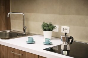 Een keuken met een wit aanrecht, een roestvrijstalen spoelbak, een plant in pot, twee blauwe kopjes en een koffiezetapparaat.
