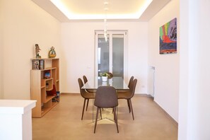 A modern dining area with a glass table, four chairs, and a wooden bookshelf.