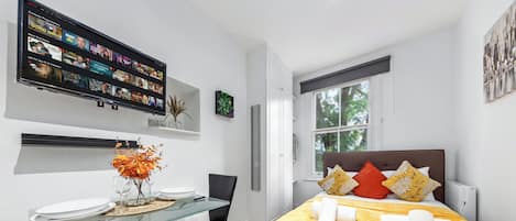 A modern bedroom with a bed, a TV mounted on the wall, a glass table, and a window.