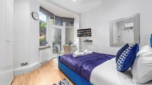 A modern bedroom with a large bed, a desk, and a window with a view of greenery. - Immaculate 1-bed Studio in London (London)
