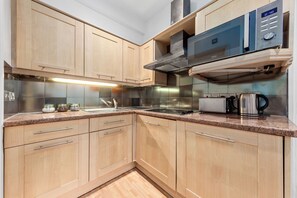 A modern kitchen with wooden cabinets, a microwave, and a coffee maker. - Immaculate 1-bed Studio in London (London)