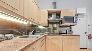 A modern kitchen with wooden cabinets, a stainless steel sink, a microwave, and a toaster. - Immaculate 1-bed Studio in London (London)