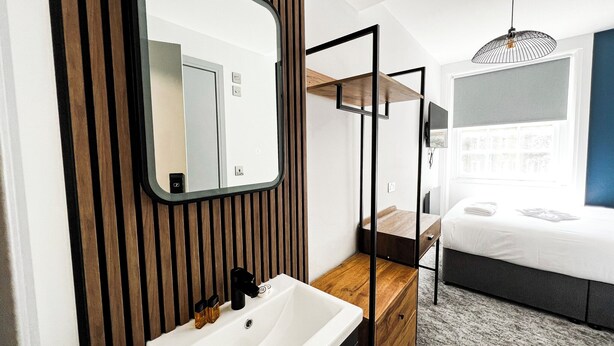 A modern bathroom with a wooden vanity, a white sink, and a mirror. - Argo Hotel - Kings Cross (London)