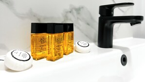 A bathroom sink with a black faucet, three bottles of orange grove bath and shower gel, and two white soap dispensers. - Argo Hotel - Kings Cross (London)
