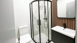 A modern bathroom with a glass-enclosed shower, a white toilet, and a wooden vanity with a mirror. - Argo Hotel - Kings Cross (London)