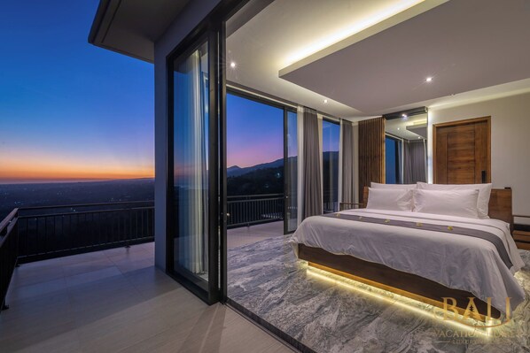 A modern bedroom with a large bed, a balcony with a city view, and a sliding glass door leading to a balcony.